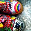 Colorful patterned shoes with red checkered bows, rainbow stripes, and a black spider design on a textured background.
