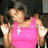A person in a bright pink sleeveless top with a white cross pendant, arms raised in a celebratory pose against a dark background.