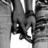 Black-and-white pixelated image of a figure with dark hair and a light-colored garment, partially obscured by vertical lines and pixelation.