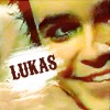 A close-up of a person's face with a red headband, green eyes, and a smiling expression, featuring the text 'LUKAS' in bold red letters on a white banner.