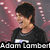 A person with short dark hair in a black shirt appears in three with text overlays reading 'Adam Lambert', 'The Next', and 'American Idol' against a pink and gray background