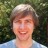 Pixelated static image of a person with light brown hair and a light blue shirt against a blurred green background.