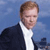 Pixelated image of a person with light brown hair wearing a dark jacket over a white shirt against a blue background.