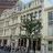 Pixelated static image of a building facade with multiple windows and a tree in front, rendered in muted tones.