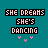 Pixelated text 'SHE DREAMS SHE'S DANCING' in black-outlined white letters above pink heart symbols on a teal background.