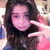 A person with long dark hair wearing a blue and pink top makes a peace sign with their right hand in a of four
