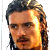 Static pixelated image of a man's face with long hair and beard, rendered in warm tones on a white background.