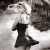 A pixelated grayscale image shows a figure in a black dress with arms raised against a light background, partially obscured by dark shapes.