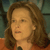 Pixelated close-up of a person with light brown hair wearing an orange garment against a blurred background.