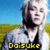 Pixelated image of a person with light hair and beard wearing dark clothing against blue sky and green field background, yellow text at bottom.