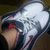 A white athletic shoe with red and dark blue accents is shown in a close-up view, with a foot partially visible inside.