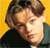 Pixelated close-up of a person with light brown hair against a solid yellow background, wearing dark clothing with a visible collar.