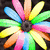 A colorful flower-shaped icon with multicolored petals in pink, blue, green, yellow, and orange radiating from a dark center against a black background.