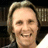 A pixelated portrait of a smiling person with light brown hair against a dark bookshelf background, accompanied by blue text labels.