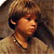 Pixelated static image of a person with brown hair and light skin wearing a beige top, viewed from the shoulders up against a dark background.