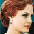 Pixelated close-up of a person with light skin and brown hair styled in a side-swept wave, wearing a white top against a teal background.