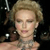 A pixelated close-up of a person with light brown hair styled in an updo, wearing a strapless dress and large earrings against a dark background.