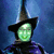 Pixelated character with glowing green face and black pointed hat against blue background, next to green text reading "Defy Gravity!" on black background.