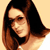 Pixelated static image of a woman with long dark brown hair and light skin, wearing a black top against a beige background.
