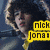 Pixelated image of a person with dark hair and light skin, wearing a yellow shirt, holding up one finger against a blue background with text reading "Nikhil Jonai" in black letters on yellow rectangles.