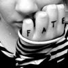 Black-and-white close-up of a person's hand with fingers spelling 'FATE' in capital letters, wearing striped clothing and partially visible face.