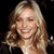 Static pixelated image of a smiling woman with long wavy blonde hair against a black background, rendered in low-resolution 256x256 pixels.