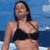 Pixelated static image of a woman in a black bikini top against a blue background with white cloud-like shapes.