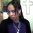Pixelated image of a person with long dark hair wearing glasses and a dark blue shirt, standing against an indistinct background.