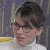Pixelated close-up of a person with dark hair wearing glasses and a white shirt against a blurred background with yellow and blue tones.