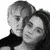 Two people in black clothing embrace; one has light hair and the other dark hair, with a hand resting on the chest.