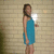 A pixelated static image shows a person in a blue sleeveless dress standing against a light brown brick wall background.