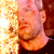 Pixelated static image of a person's face with warm orange and yellow tones on the left side, set against a dark background.