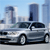 Pixelated image of a silver sedan parked in front of modern skyscrapers under a light blue sky.