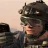 Pixelated close-up of a figure with dark curly hair wearing a dark helmet-like headpiece, set against a light gradient background with a blurred dark shape on the left.