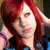 Pixelated image of a person with long red hair, light skin, and a slight smile, wearing a dark top with blue accents.