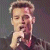 Pixelated static image of a person with light brown hair and dark clothing against a gradient background, rendered in low-resolution style typical of early internet icons.