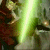 Animated sequence showing a character with light brown hair and dark clothing holding a green lightsaber, transitioning through multiple poses against rocky terrain.