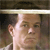 A pixelated close-up of a person's face with a light-colored headband, dark hair, and neutral expression against a blurred background.