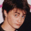 A pixelated image of a person with dark hair wearing a black jacket over a graphic shirt, partially cropped on the right side.