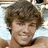 Pixelated close-up of a person with brown curly hair, light skin tone, and visible facial features including eyes, nose, mouth, and chin.