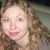 Pixelated close-up of a person with light brown curly hair, fair skin, and a neutral expression against a blurred background.