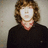 Pixelated static image of a person with shoulder-length brown hair wearing a black top against a light gray background.