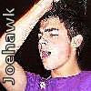 Pixelated image of a person in a purple shirt with a hand raised near their head, vertical text on the left side.