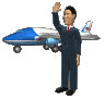 A man in a dark suit waves with his right hand while standing before a blue and white airplane on a gray background.