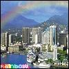 Pixelated cityscape with tall buildings, water, and mountains under a cloudy sky with a faint rainbow arc.