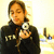 A person in a black hoodie with white text holds a silver digital camera, captured in a of four showing subtle pose variations