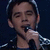 Pixelated close-up of a person singing into a microphone, wearing dark clothing with light reflections on the shoulder.