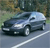 Pixelated image of a dark-colored sedan parked on a road with a blurred green background.