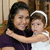 A woman in a dark purple top embraces a child in white clothing with a white headband, both smiling against a wooden background.