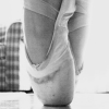 Black-and-white close-up of a ballet dancer's foot in a pointe shoe, with a checkered fabric background.